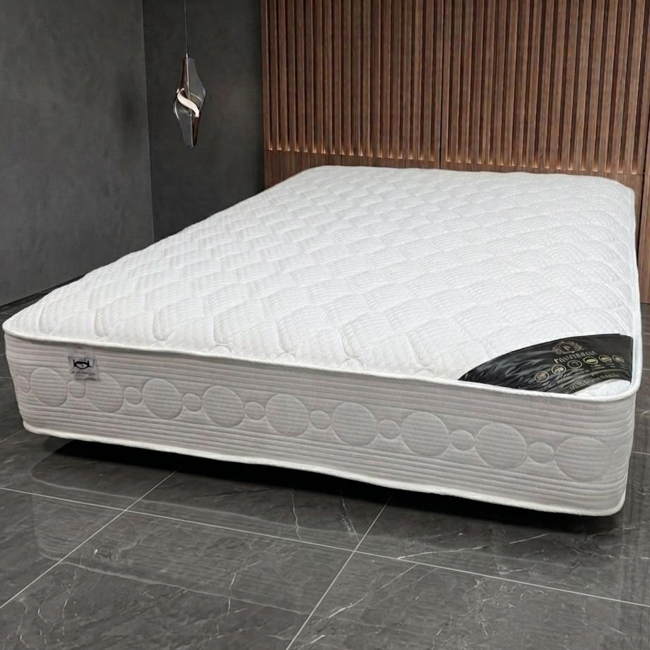 White mattress on a gray floor with a wooden headboard in the background