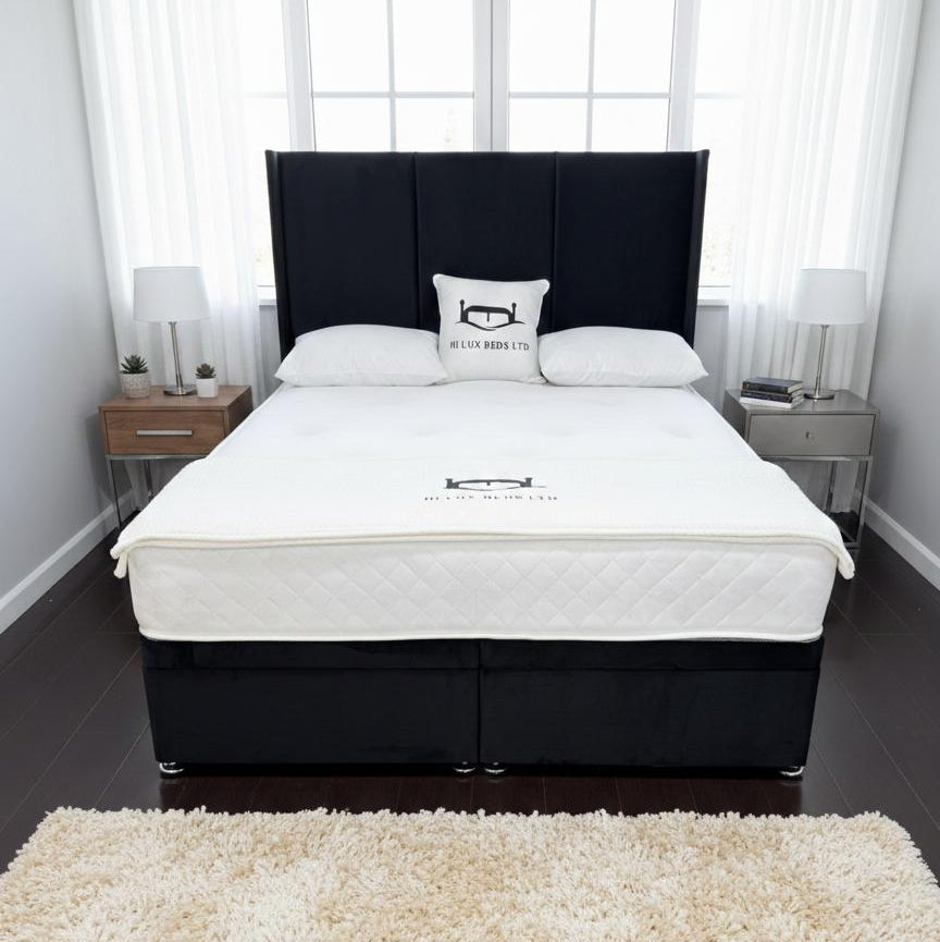 Bed with a black headboard and white mattress in a room with a rug and nightstands.