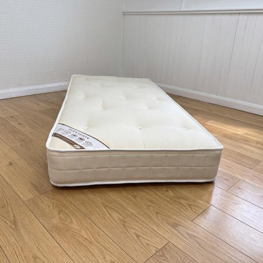 Beige mattress on a wooden floor with white walls