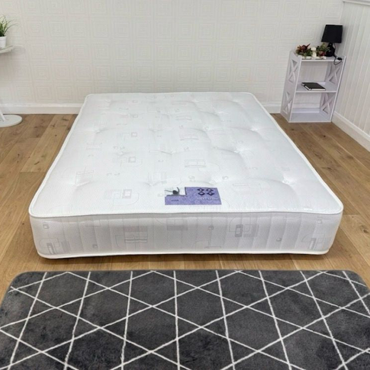 Mattress on a wooden floor with a gray rug in a room.