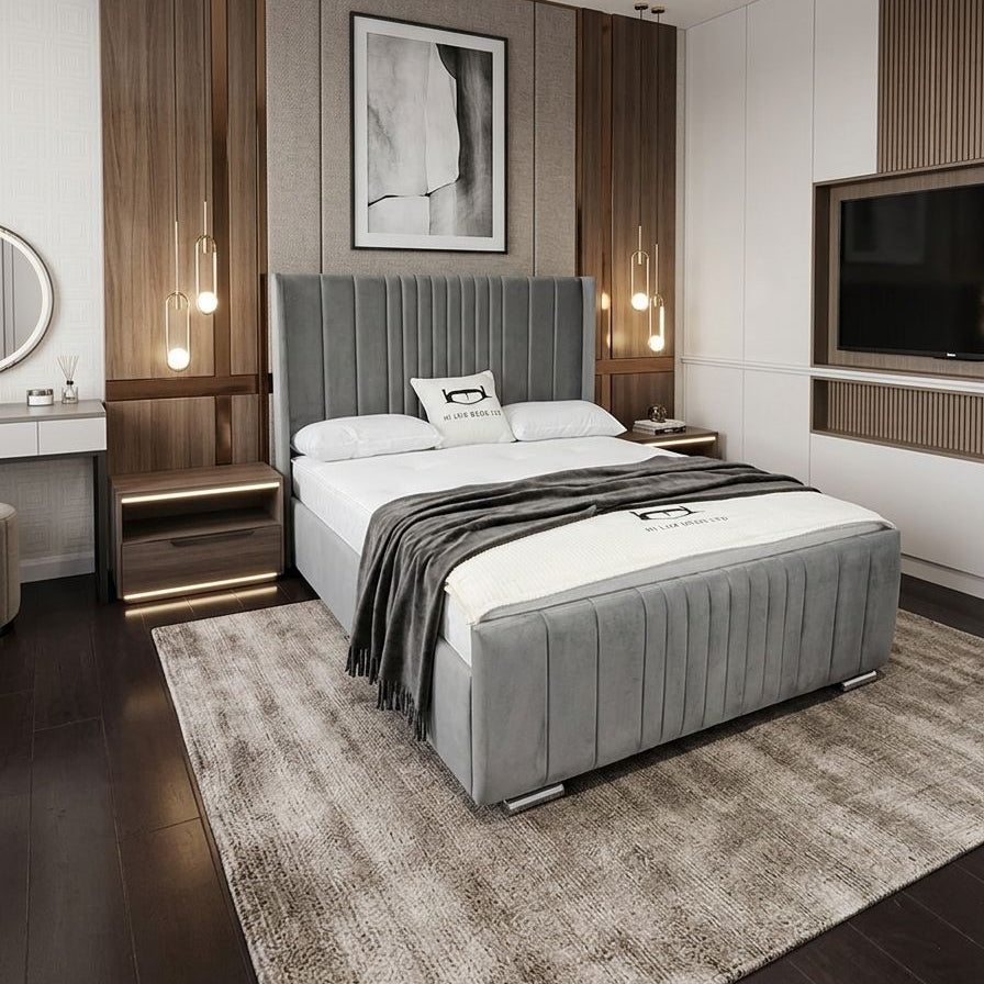 Modern bedroom with gray upholstered bed, wooden cabinets, and a television.