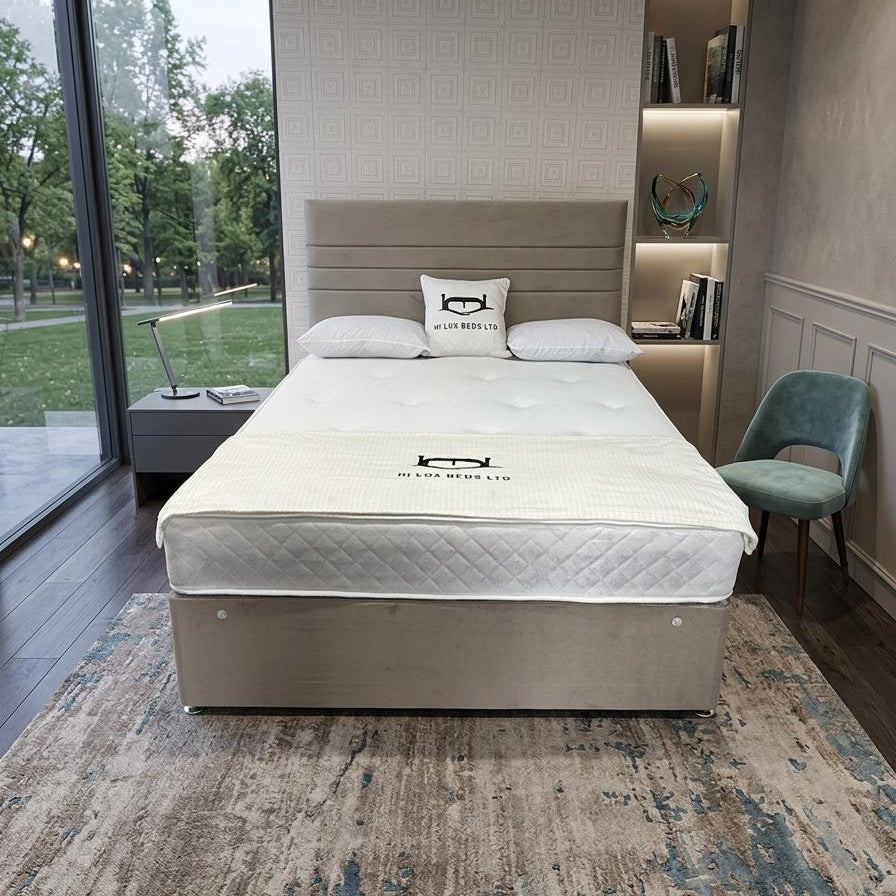 A modern bed frame with a quilted white mattress and matching pillows, styled in a contemporary bedroom with a patterned rug, built-in shelving, and a green chair.