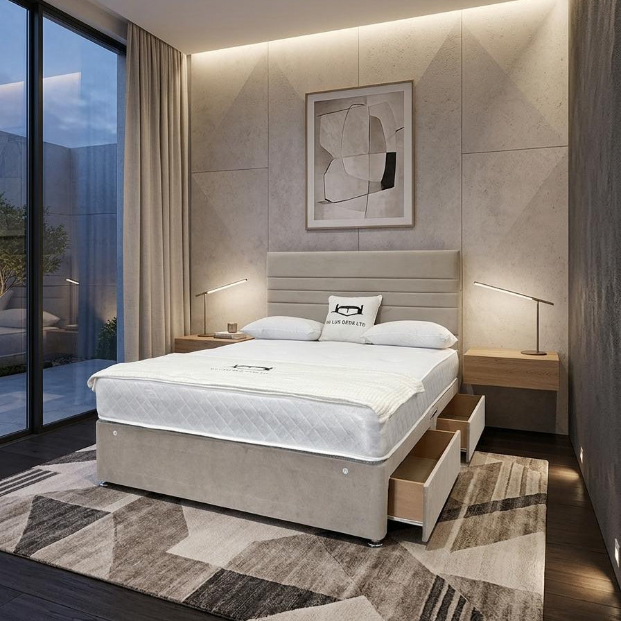 A modern bedroom featuring a beige upholstered bed with a white mattress, set on a geometric patterned rug. The room has a textured beige wall with integrated LED lighting, two wooden nightstands with lamps, and a large window looking out onto a patio at dusk.