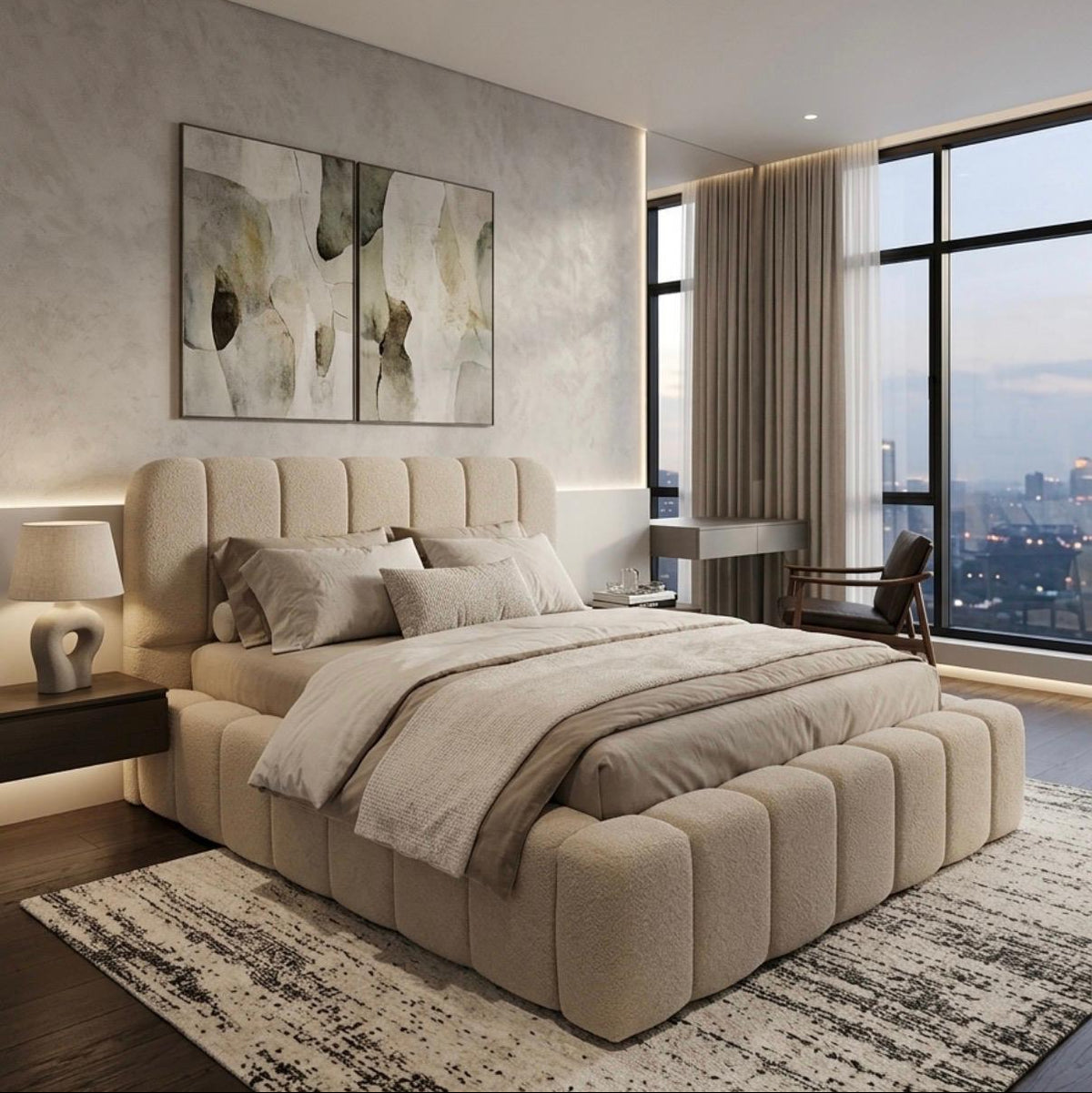 A modern bedroom featuring a large beige tufted platform bed with a matching upholstered footboard, styled with neutral beige bedding. The room has a textured light gray wall with abstract wall art, a black nightstand with a lamp, and a large floor-to-ceiling window overlooking a city skyline at dusk.