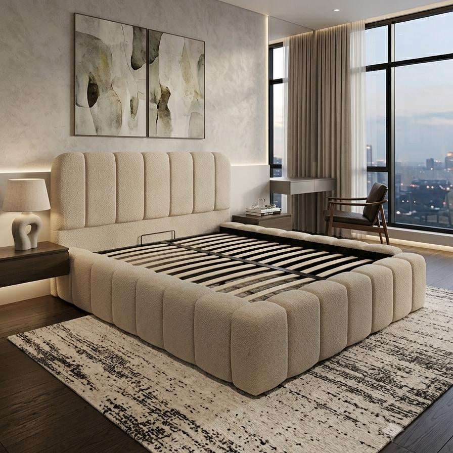A modern bedroom featuring a low, tufted platform bed in a light beige fabric, styled with a black slatted base. The room has a textured light gray wall with abstract wall art, a dark wood nightstand, and a large window with a view of a city skyline at dusk.