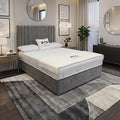 A modern bedroom featuring a gray upholstered bed frame with a white mattress, styled with a gray and white geometric area rug, bedside tables, wall art, and mirrors.