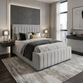 A modern bedroom featuring a light gray tufted upholstered bed frame with a matching headboard, styled with gray and black bedding, a gray patterned rug, and contemporary wall lighting.