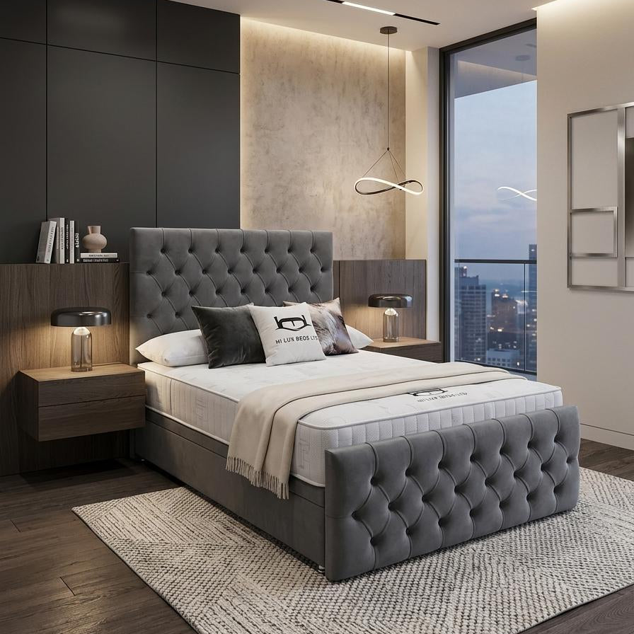 A modern bedroom featuring a gray tufted upholstered bed frame with a matching headboard and footboard, styled with white and gray bedding, flanked by dark wood nightstands and a textured rug.