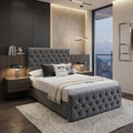 A modern bedroom featuring a gray tufted upholstered bed frame with a matching headboard and footboard, styled with white and gray bedding, flanked by dark wood nightstands and a textured rug.