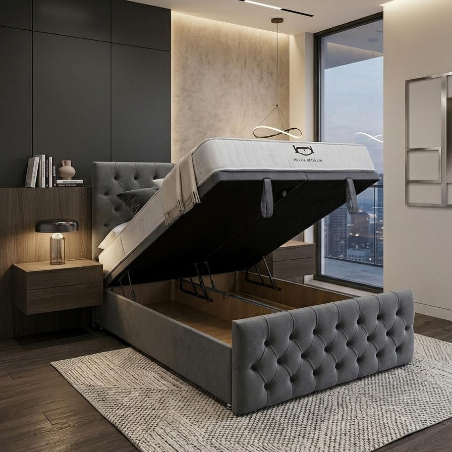 A modern gray tufted lift-up bed frame with its mattress and bedding raised to show the storage compartment underneath, set in a contemporary bedroom with dark wood flooring, a textured rug, and a large window.