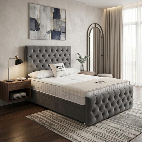 A modern bedroom featuring a gray tufted upholstered bed frame with a mattress, styled with a wooden nightstand, black desk lamp, abstract wall art, and a striped area rug.