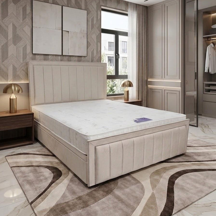 A modern upholstered bed frame with a tall paneled headboard and a white mattress, shown in a styled bedroom with patterned wallpaper, a rug, bedside tables, lamps, and a walk-in closet.